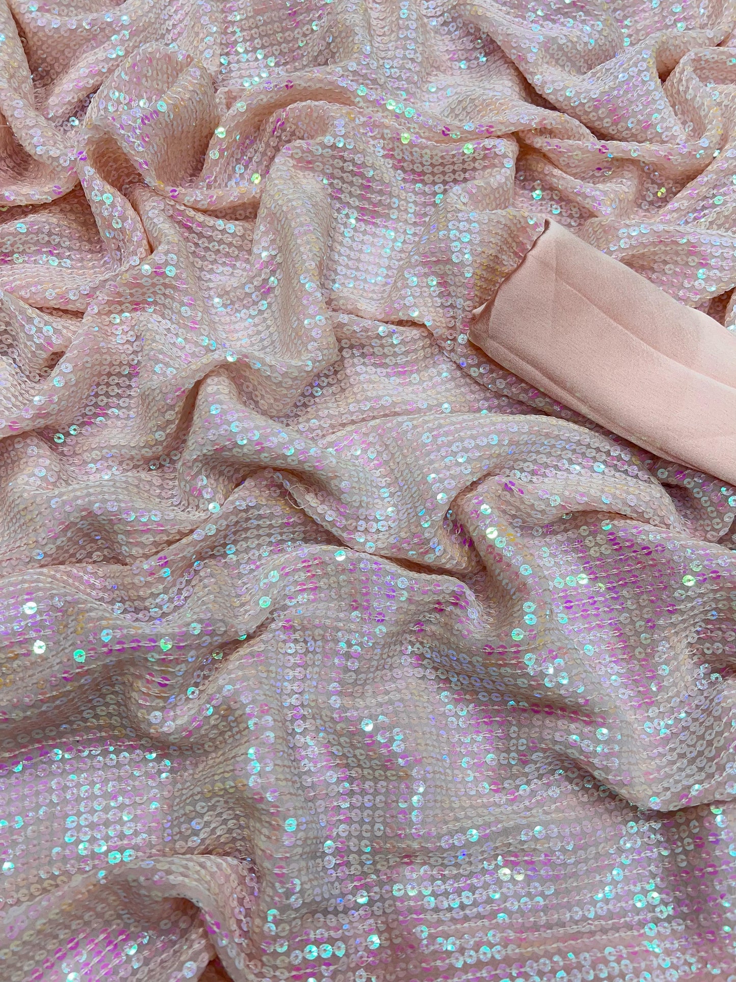 A close-up of the Baby Pink Fully Sequins Bollywood Style Saree with Stitched Blouse features shimmery light pink and iridescent sequins, adding a sparkling effect. The slightly gathered fabric enhances texture, while a folded plain pink cloth on the right complements its elegance.
