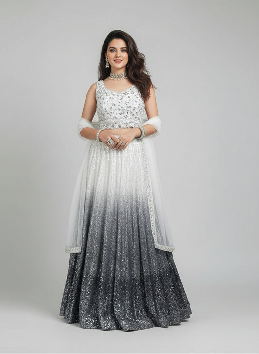 Woman in a silver and white traditional outfit standing in front of a glass architectural structure.