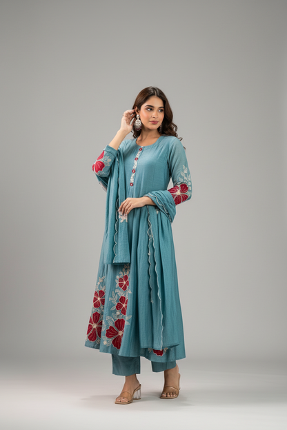 Woman wearing a teal embroidered outfit against a dark green background