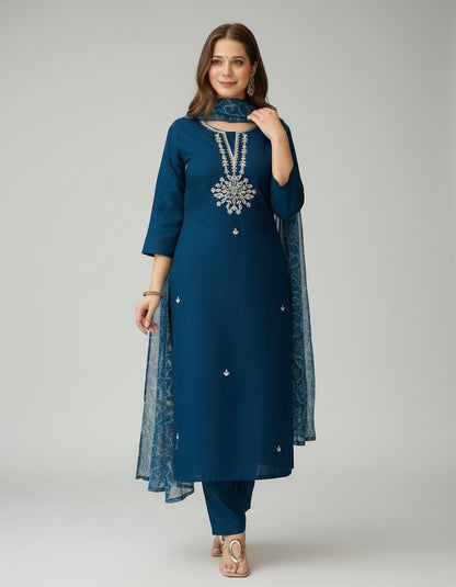 Woman wearing a blue traditional outfit with a necklace, standing outdoors.