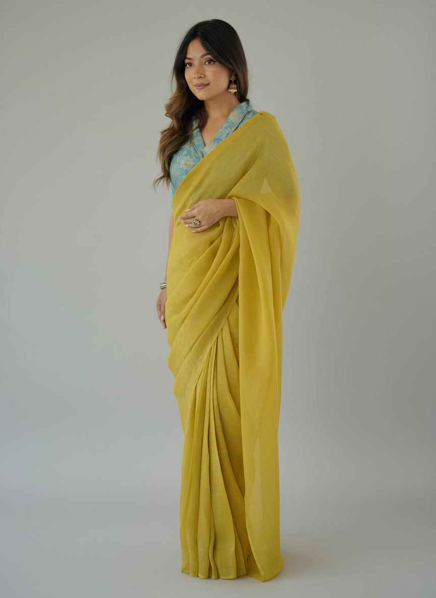 Woman wearing a yellow saree with a blue blouse against a white background