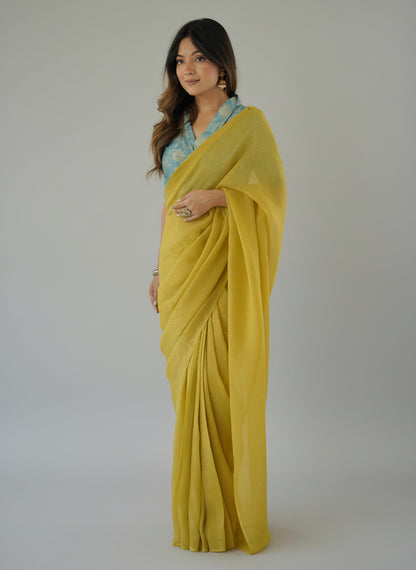 Woman wearing a yellow saree with a blue blouse against a white background