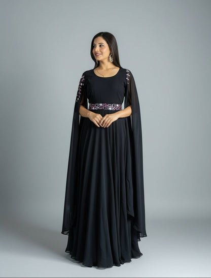 Woman in a black evening gown with a sheer overlay standing against a textured purple curtain.