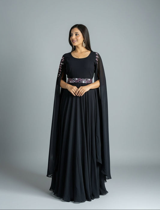 Woman in a black evening gown with a sheer overlay standing against a textured purple curtain.