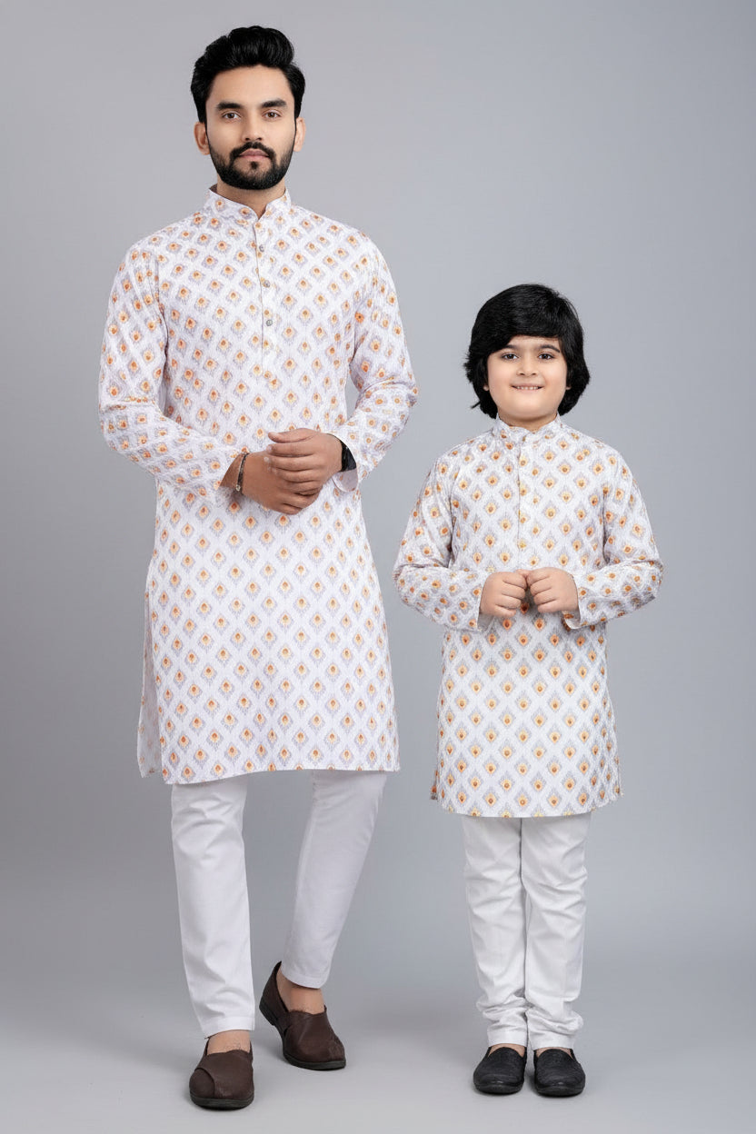 Man and child wearing matching white kurta sets with orange patterns, sitting on a stool against a beige background.