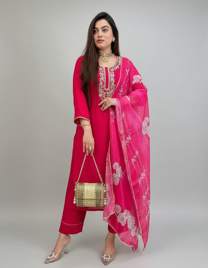 Woman in a red outfit with a pink dupatta standing against a green wall.