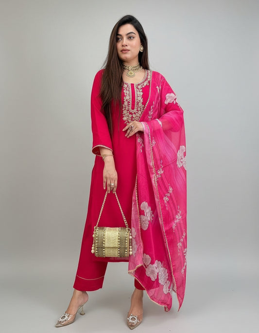 Woman in a red outfit with a pink dupatta standing against a green wall.
