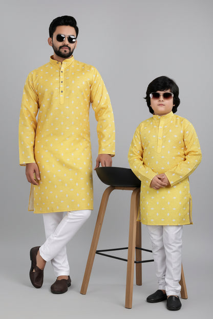 Man and child wearing matching yellow kurta sets with white pants against a beige background.