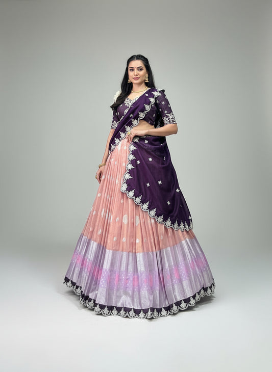 Person wearing a traditional outfit with a purple and pink saree in an indoor setting.