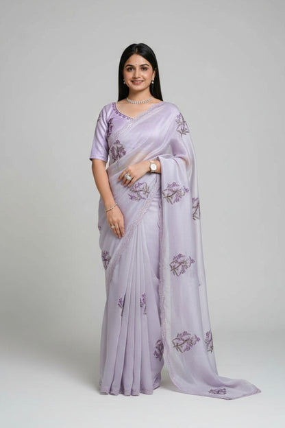 Woman in a light purple saree with floral patterns standing outdoors.