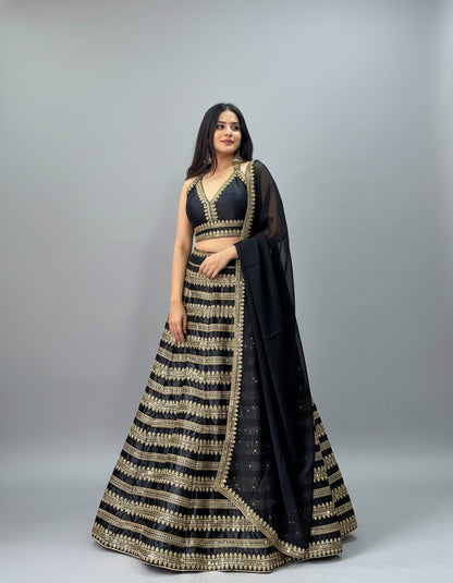 Woman in a black and gold traditional outfit standing indoors with decor elements.