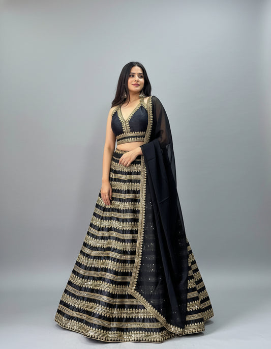 Woman in a black and gold traditional outfit standing indoors with decor elements.