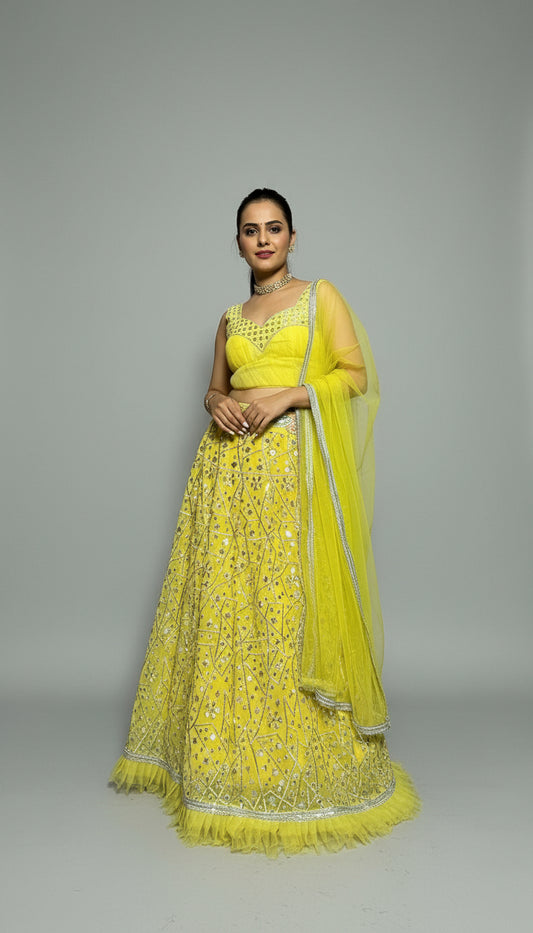 Woman in a bright yellow traditional outfit with a matching dupatta against a plain background