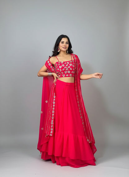 Woman in a bright pink traditional outfit with floral patterns, standing indoors.